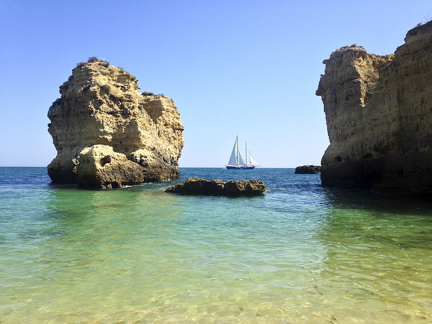 Sailboat Between Coastal Cliffs in Clear Blue Sea