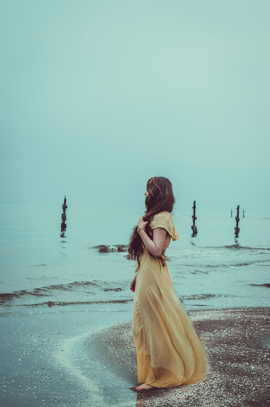 Woman in Yellow Dress Standing on Moody Beach Shore
