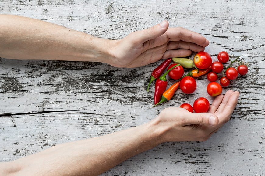 Hands holding fresh tomatoes and peppers on rustic wood