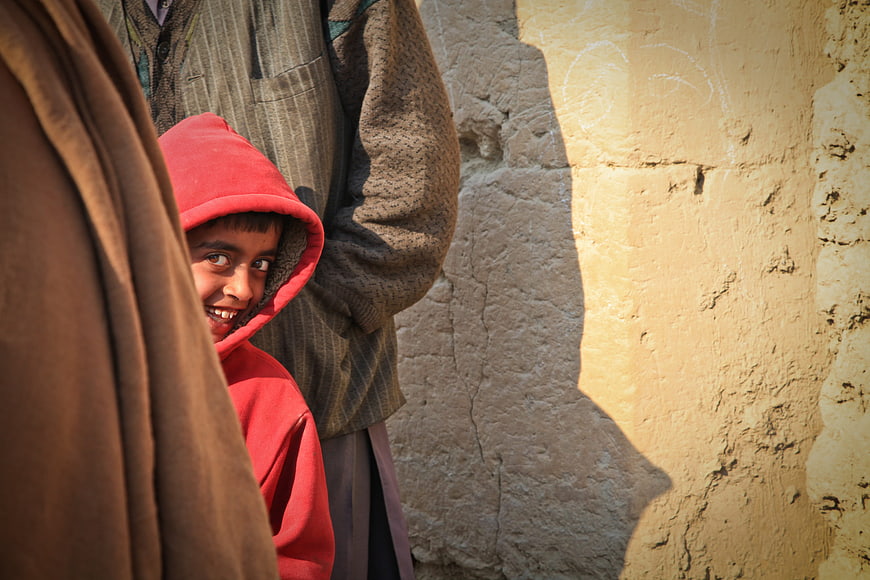 Smiling Afghan boy in red hoodie peeking from behind