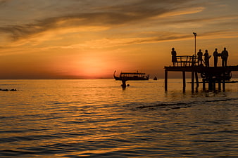 Silhouetted People on Pier Watching Golden Sunset Over Ocean