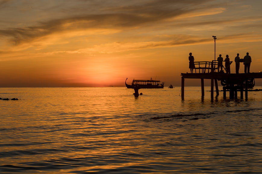 Silhouetted People on Pier Watching Golden Sunset Over Ocean