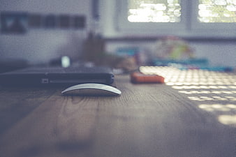 Close-up of computer mouse on wooden desk with blurred laptop