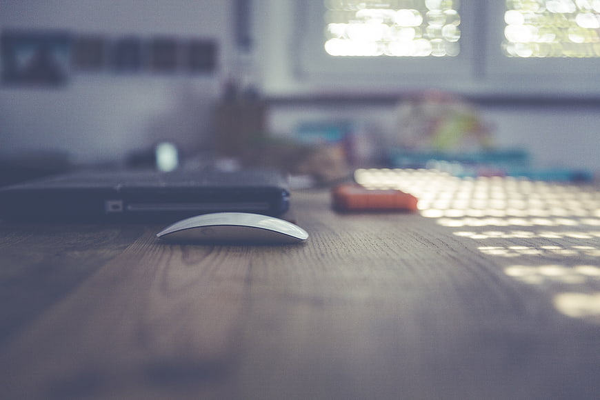 Close-up of computer mouse on wooden desk with blurred laptop