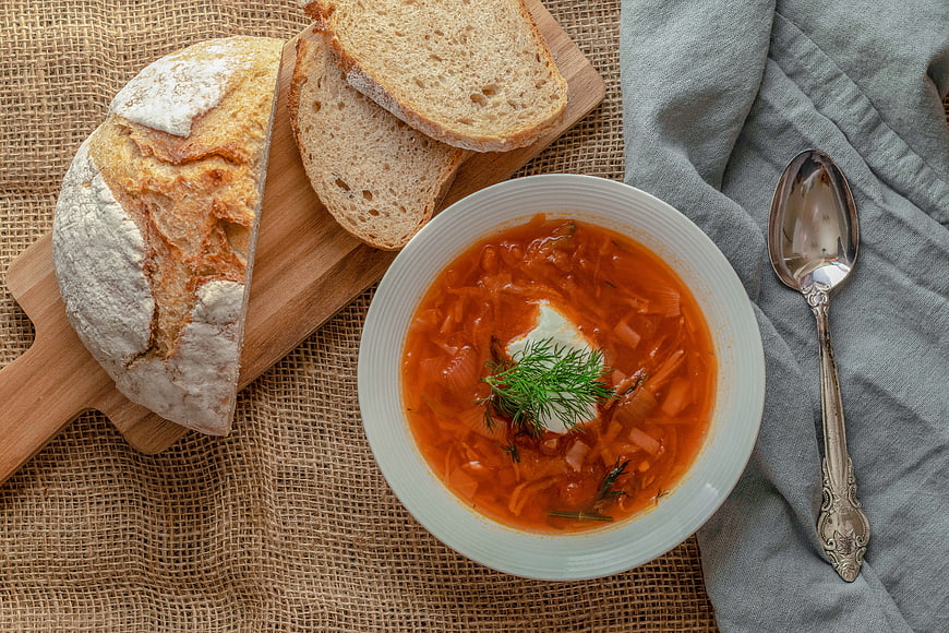 Top view of borscht soup with sour cream and fresh bread on rustic table