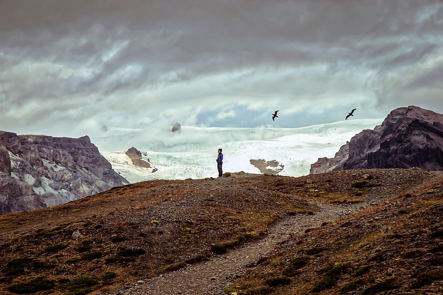 Woman standing on rocky ridge overlooking glacier and mountains