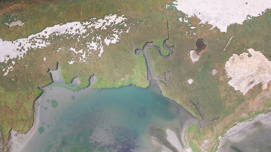 Aerial view of arctic coastline with snow patches and river delta