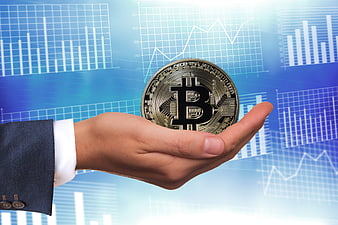 Hand holding physical Bitcoin coin against financial charts