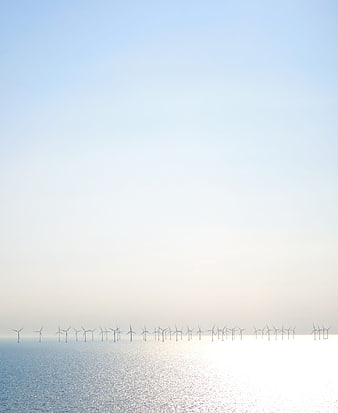 Offshore wind turbines on calm ocean horizon under clear blue sky