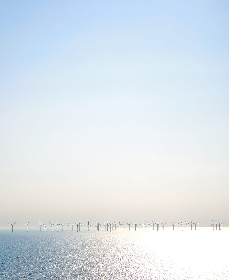 Offshore wind turbines on calm ocean horizon under clear blue sky