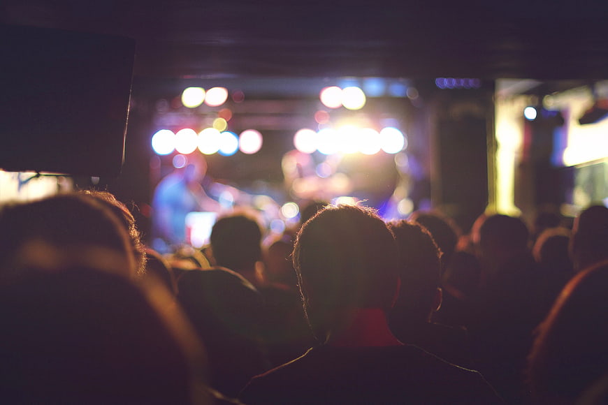 Silhouettes of crowd watching concert stage with bokeh lights