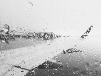 Raindrops on airplane window with blurred wing view