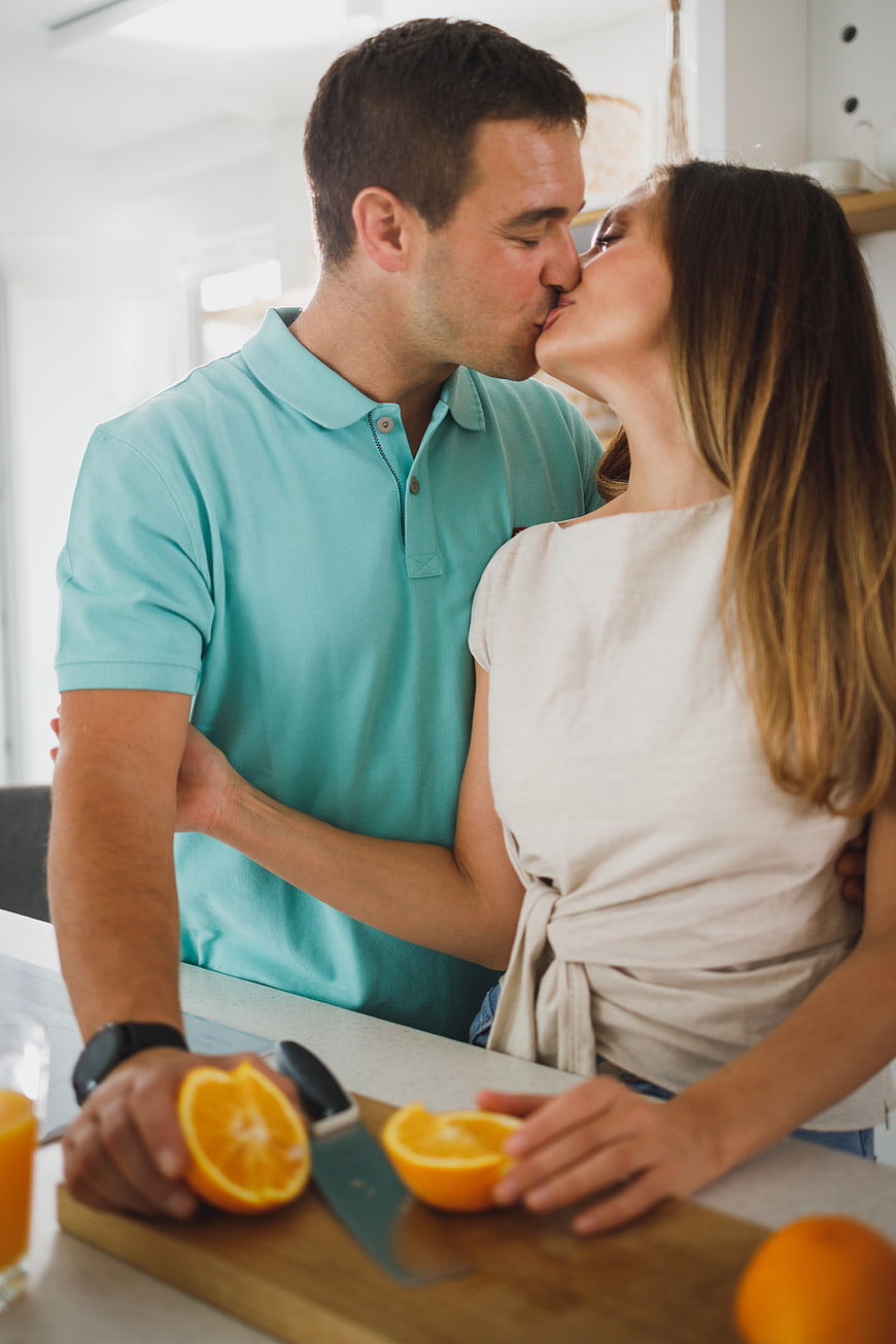 Romantic couple kissing in kitchen while preparing fresh orange juice