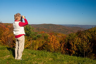 Senior woman birdwatching with binoculars in autumn landscape