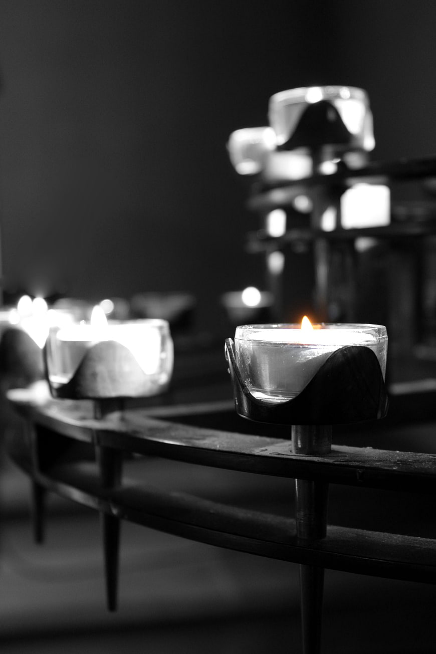 Black and white photo of lit tea light candles on a metal rack