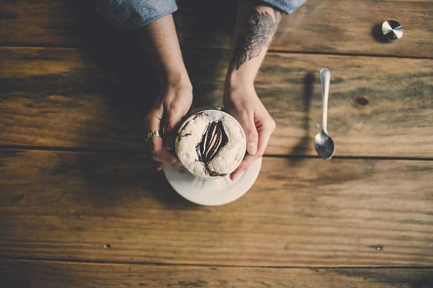 Top view of hands holding frothy cappuccino on wooden table