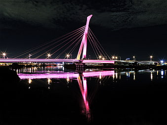 Pink illuminated cable-stayed bridge at night with water reflection