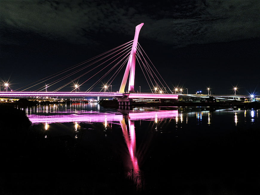 Pink illuminated cable-stayed bridge at night with water reflection