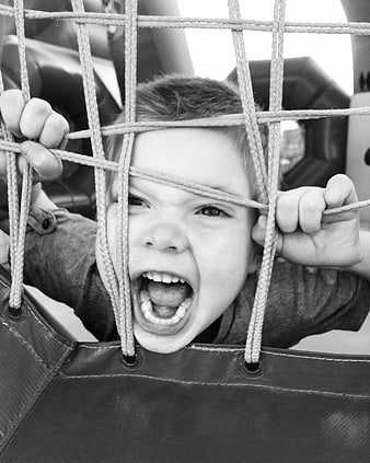 Black and white portrait of a young boy screaming through a rope net