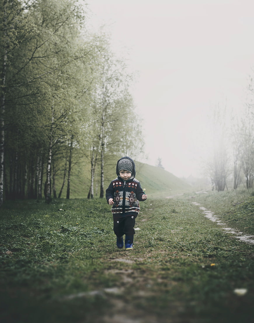 Toddler running on grassy path in foggy birch forest
