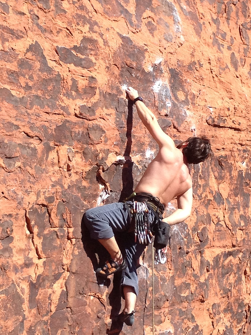 Shirtless Rock Climber Scaling Red Sandstone Cliff