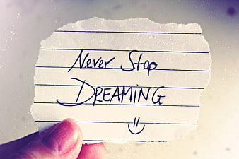 Hand holding torn paper note saying never stop dreaming