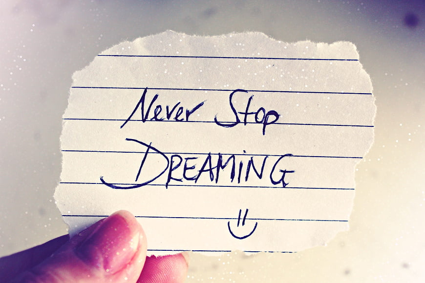 Hand holding torn paper note saying never stop dreaming