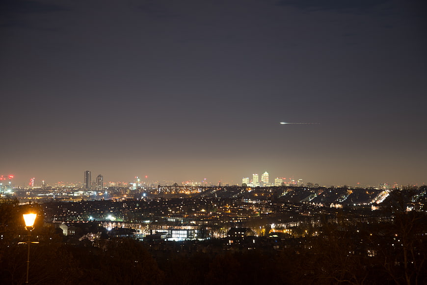 London City Skyline at Night with Airplane Trail