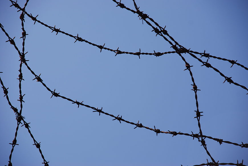 Silhouette of Barbed Wire Fence Against Blue Sky