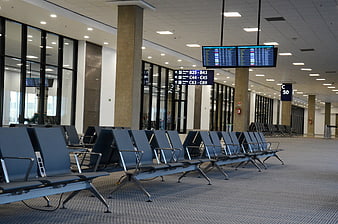 Empty airport terminal waiting area with blue seats and flight information screens