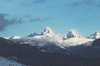 Snowy Mountain Peaks with Forested Slopes and Blue Sky