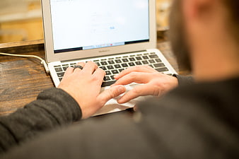 Man Typing on Laptop at Wooden Desk