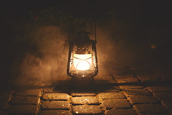 Vintage oil lamp glowing on cobblestone path at night
