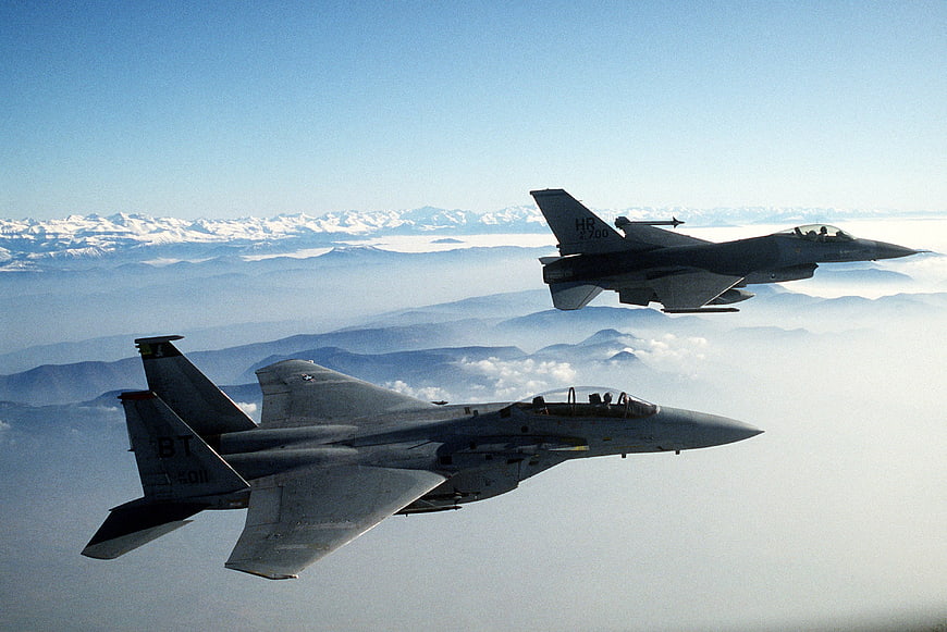 Two Military Fighter Jets Flying In Formation Over Snowy Mountains