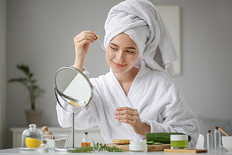 Woman applying serum with dropper in white bathrobe