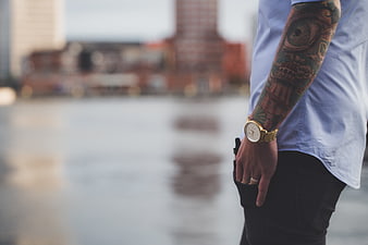 Man with tattooed arm wearing gold watch by waterfront