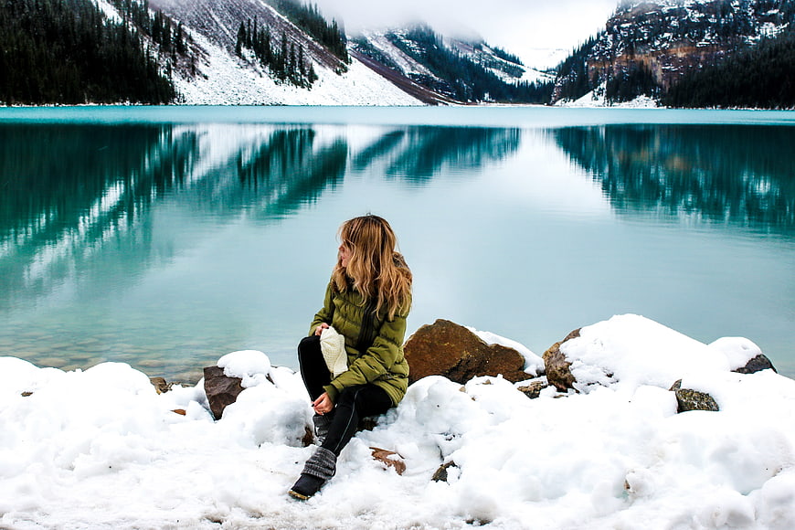 Woman sitting by turquoise lake in snowy mountains