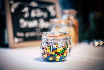Colorful candies in glass jar on white table