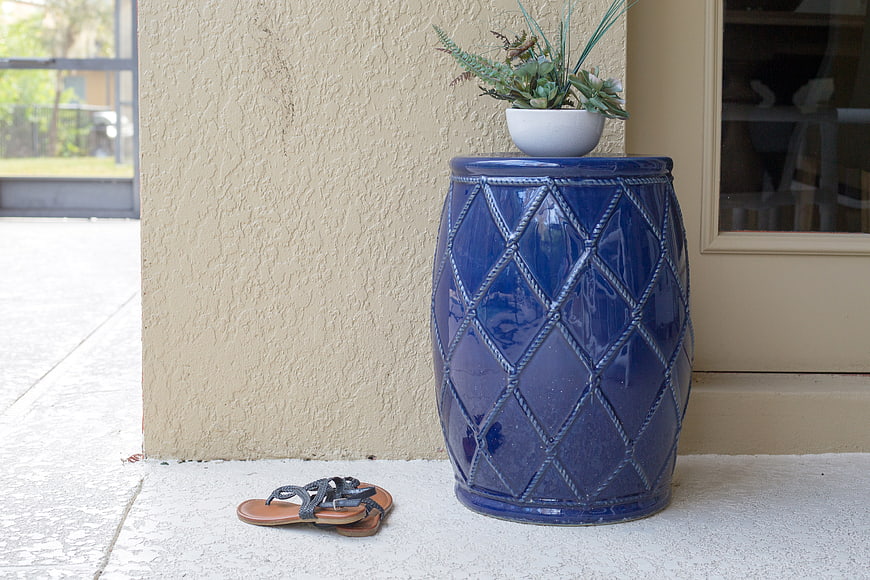Blue ceramic garden stool with plant and sandals on patio
