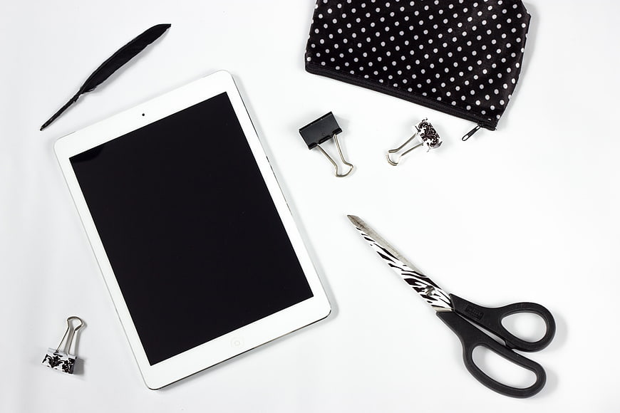 Flat lay of white tablet, scissors, and office accessories on white background