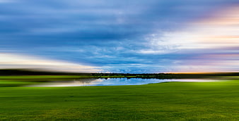 Panoramic landscape of green field and lake with dramatic sky