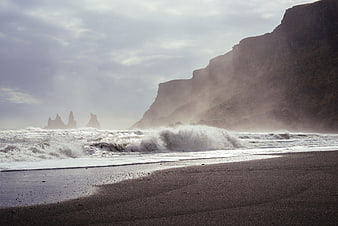 Dramatic black sand beach with crashing waves and distant sea stacks