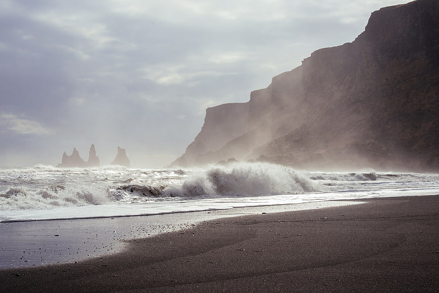 Dramatic black sand beach with crashing waves and distant sea stacks