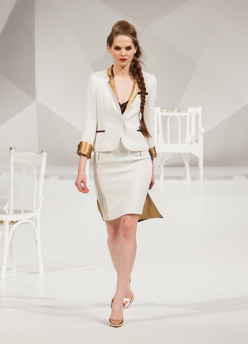 Female model walking runway in white and gold designer suit