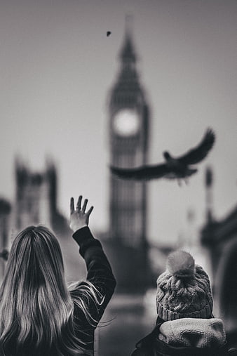 Woman and child watching bird fly past Big Ben in black and white