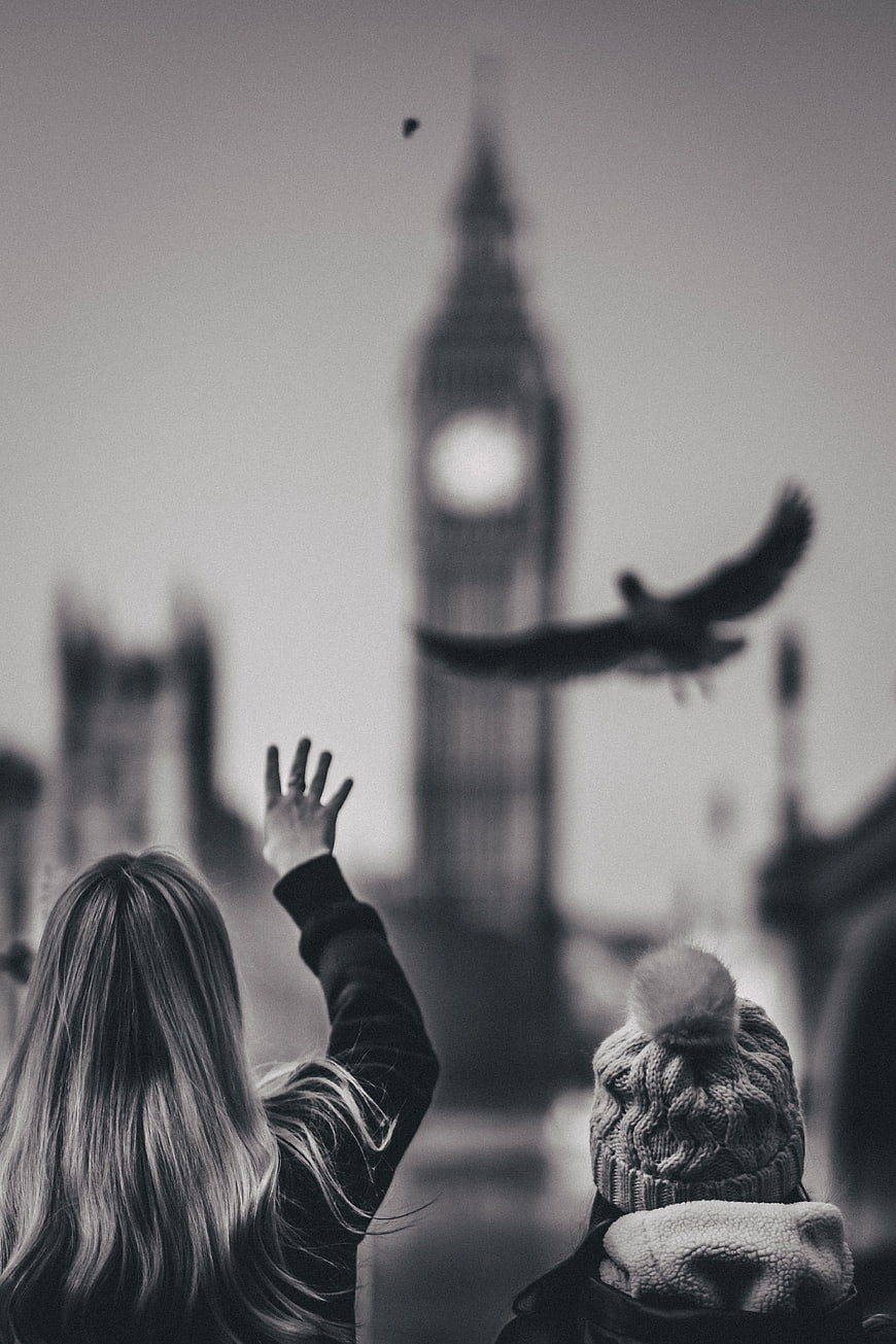 Woman and child watching bird fly past Big Ben in black and white