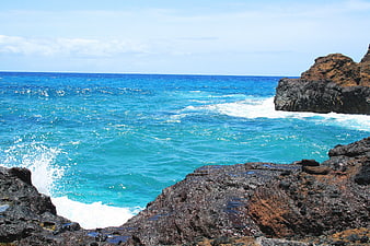 Turquoise ocean waves crashing against dark volcanic rocks