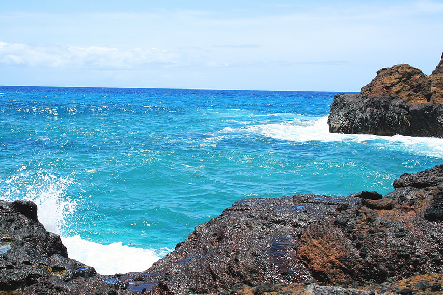 Turquoise ocean waves crashing against dark volcanic rocks