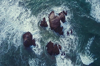 Aerial View of Dark Rocks in Turbulent Ocean Waves