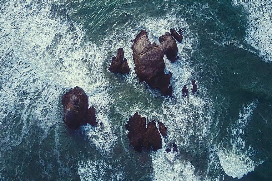 Aerial View of Dark Rocks in Turbulent Ocean Waves